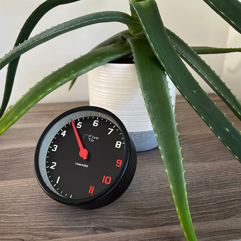 FiveTo Desktop Tacho Clock with plant. Timekeeping redesigned in the style of a sports car rev counter. Exclusively available from www.fiveto.co.uk
